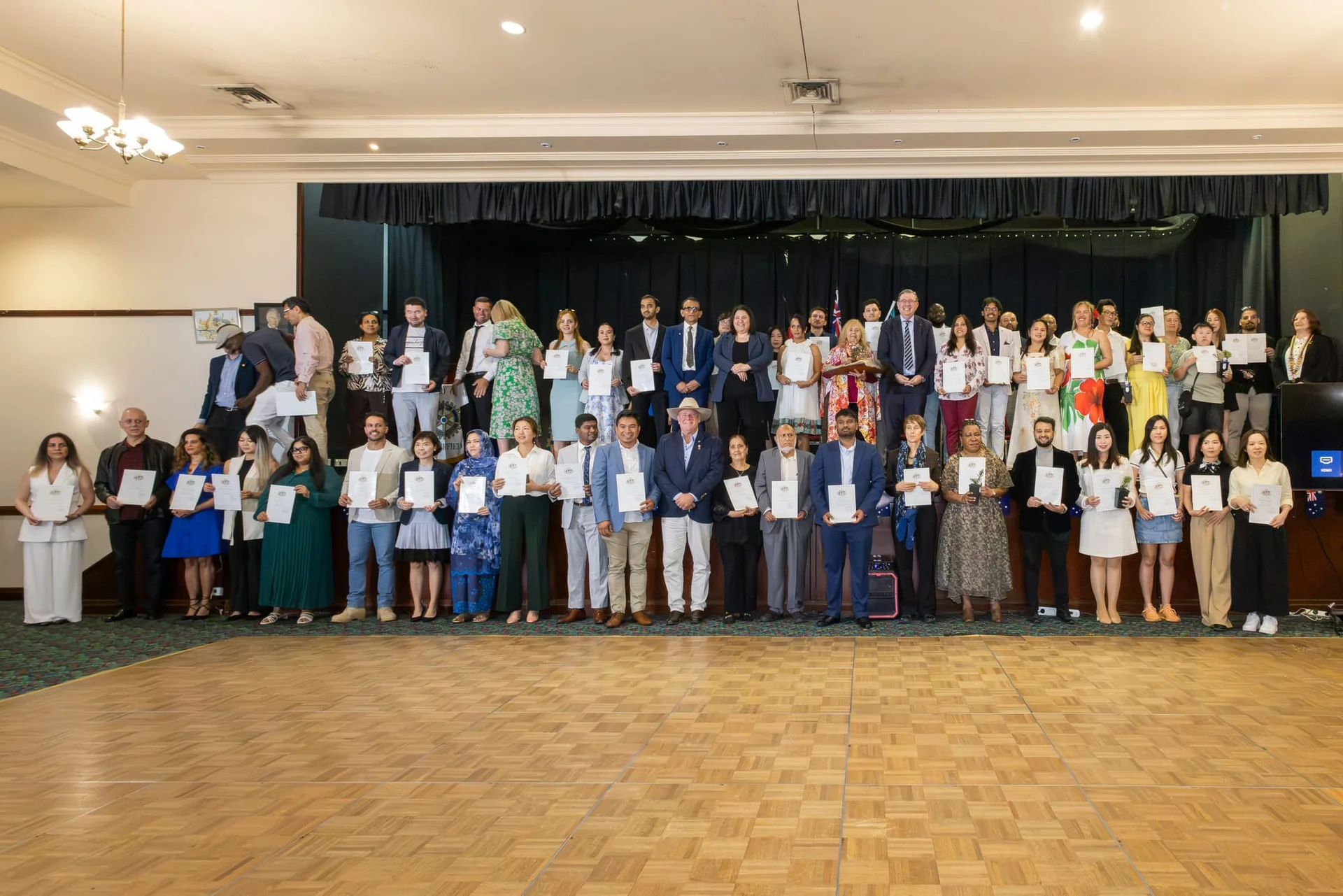 New Australian citizens holding their citizenship certificates on stage at Souths Sports Club, Acacia Ridge