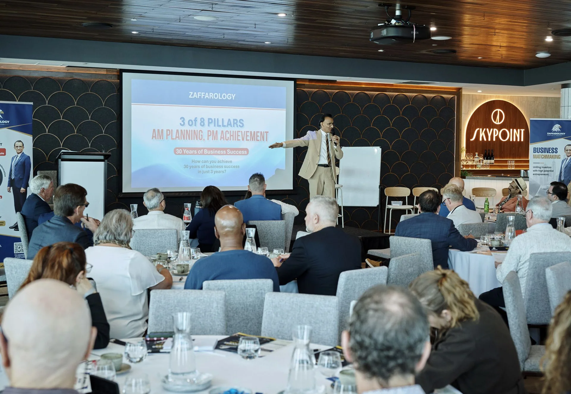 Zaffar Khan presenting the slide AM Planning PM Achievement, with the SkyPoint sign behind him