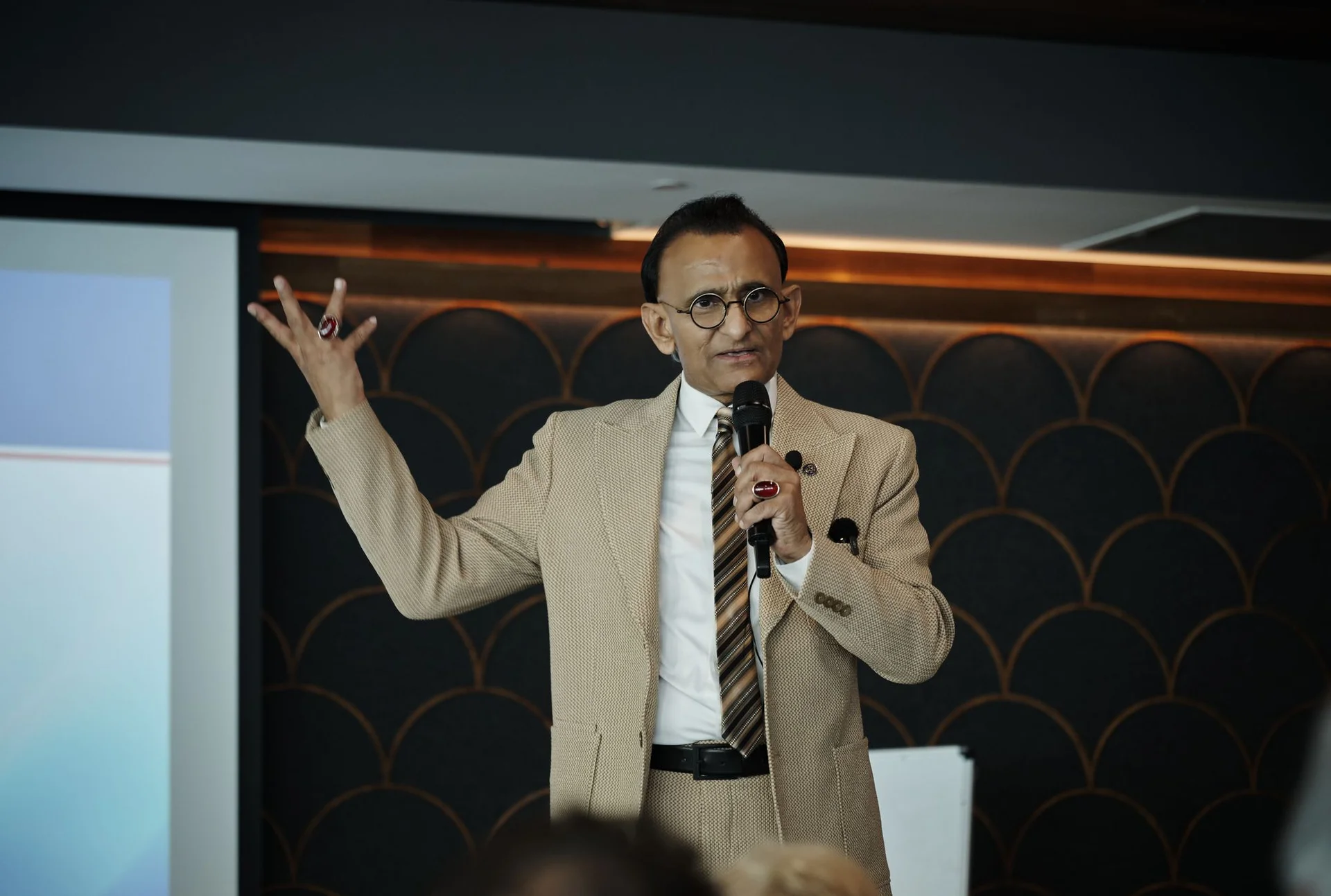Zaffar Khan with both arms raised, making a point to the room