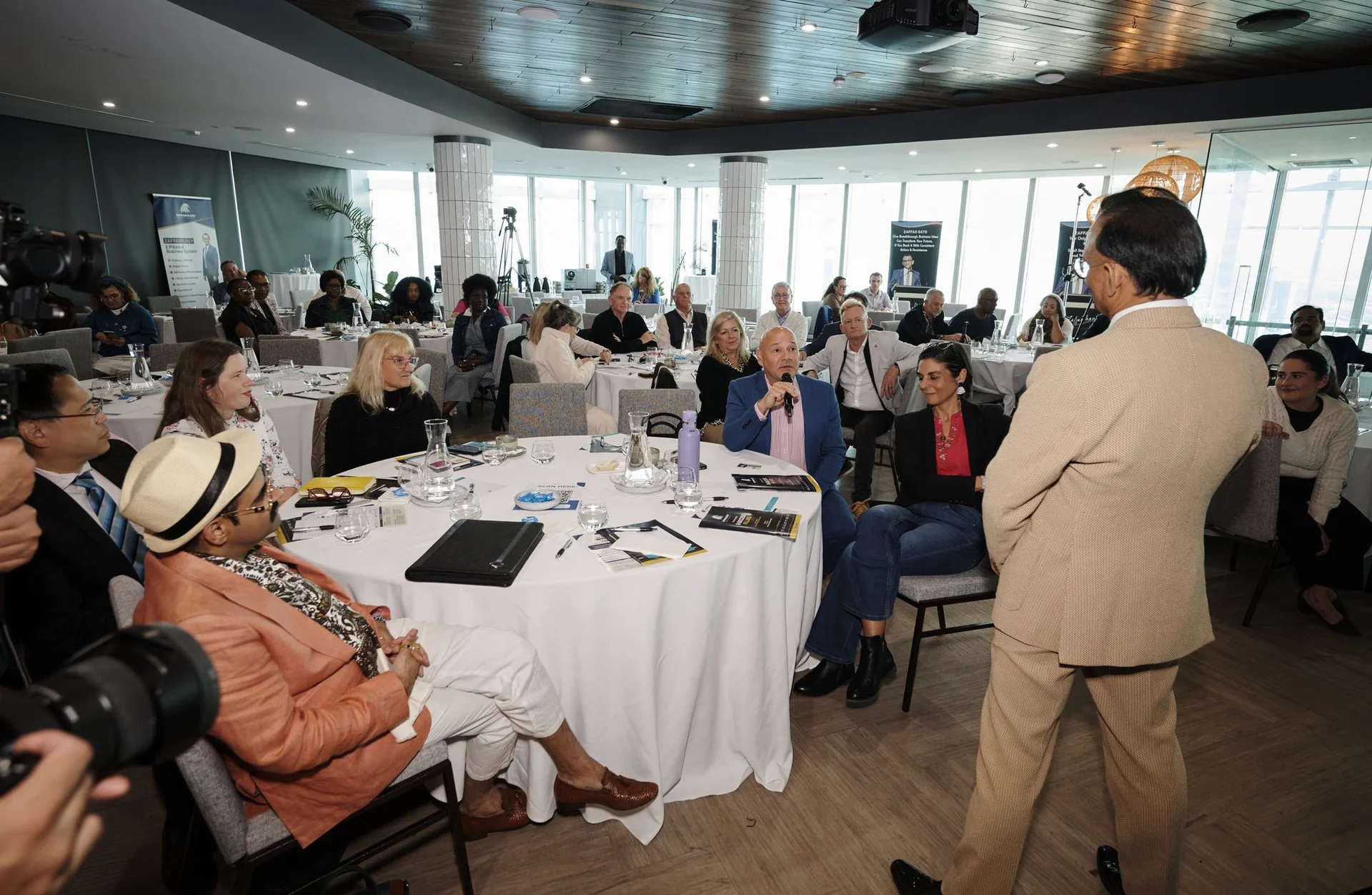 Zaffar Khan walking to a table as an attendee speaks into a microphone